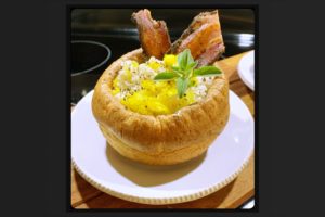 Southwest chicken and sweet onion pilaf, served in the center of a Yorkshire Pudding. The outer crust of the Yorkshire Pudding, also called a popover, is flaky and golden brown while the center is soft and delicate. It's topped with peppered bacon, fresh chow chow and garnished with a sprig of oregano.