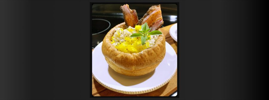 Southwest chicken and sweet onion pilaf, served in the center of a Yorkshire Pudding. The outer crust of the Yorkshire Pudding, also called a popover, is flaky and golden brown while the center is soft and delicate. It's topped with peppered bacon, fresh chow chow and garnished with a sprig of oregano.